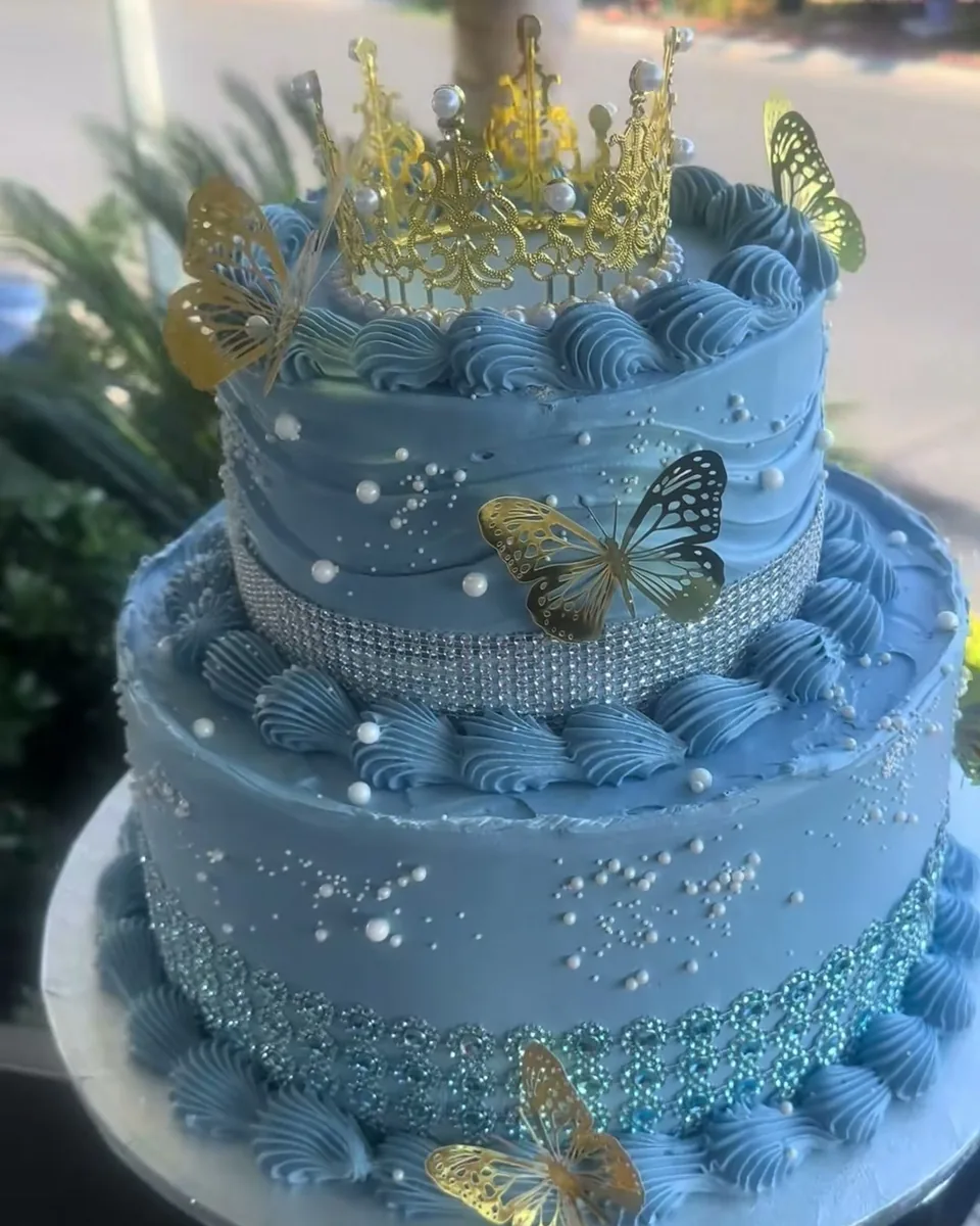 Two-tier dusty blue quinceañera cake with gold crown and butterflies